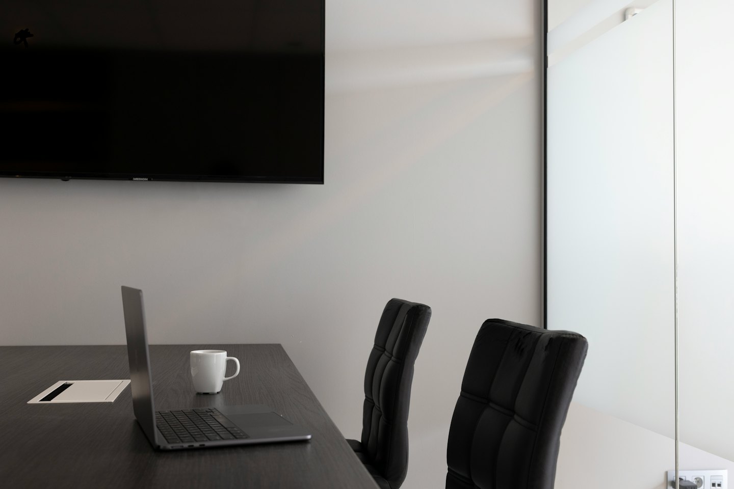 Sala de conferencias con portátil, taza y pantalla de televisión.